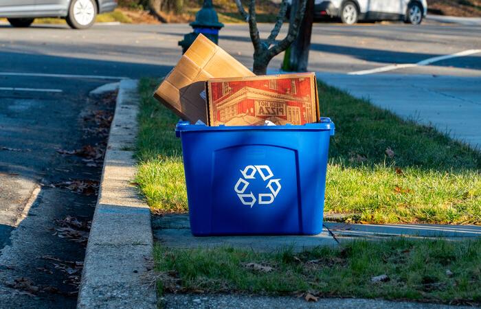 A pizza box in a blue curbside recycling bin.